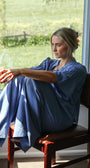 Woman sitting on a chair by a window holding a bowl, with a scenic view outside.