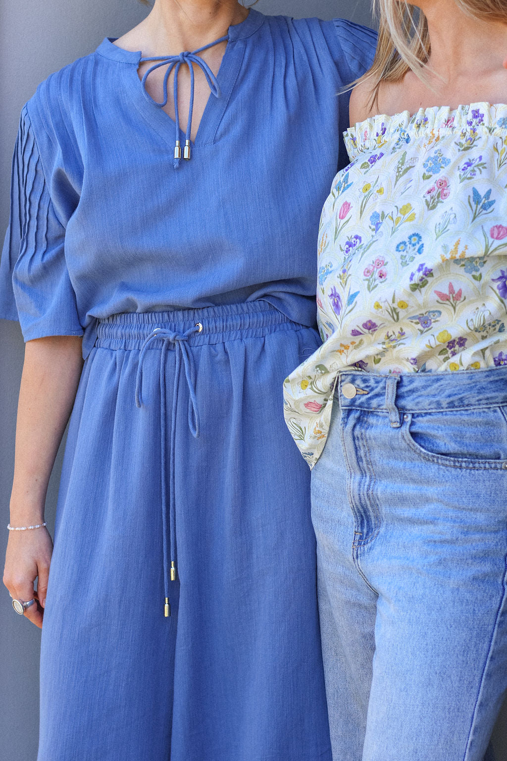 Two women wearing a blue dress and floral top with jeans.
