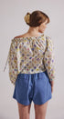 Woman wearing a floral off-shoulder top and blue shorts against a plain background