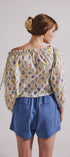 Woman wearing a floral off-shoulder top and blue shorts against a plain background