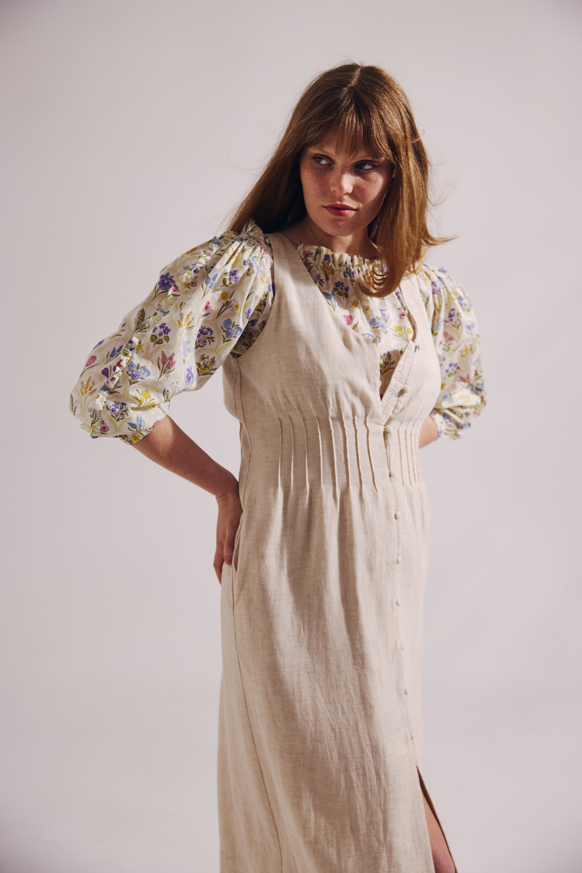 Woman wearing a floral blouse and beige dress with a white background