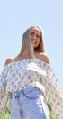 Woman wearing a floral off-shoulder top and jeans against a clear blue sky.