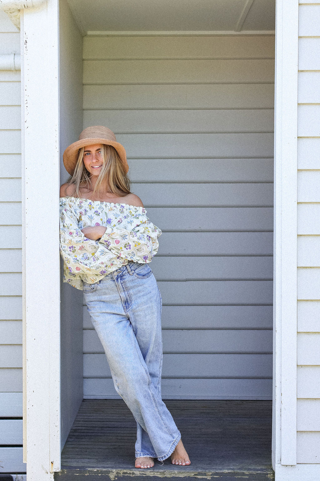 Woman wearing a floral top and jeans standing in a doorway.