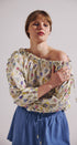 Woman wearing a floral off-shoulder top and blue skirt against a plain background