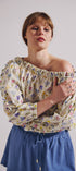 Woman wearing a floral off-shoulder top and blue skirt against a plain background