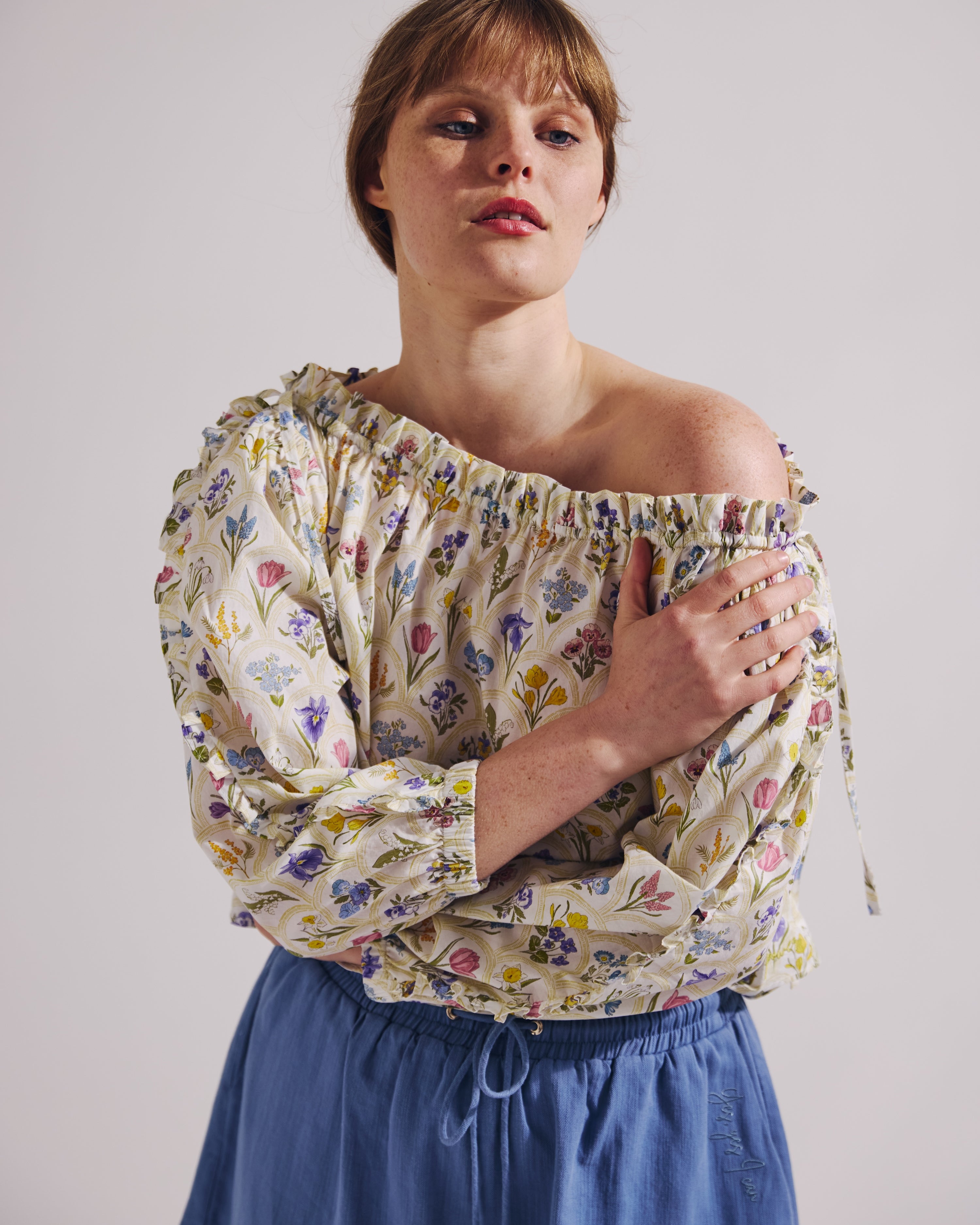Woman wearing a floral off-shoulder top and blue skirt against a plain background