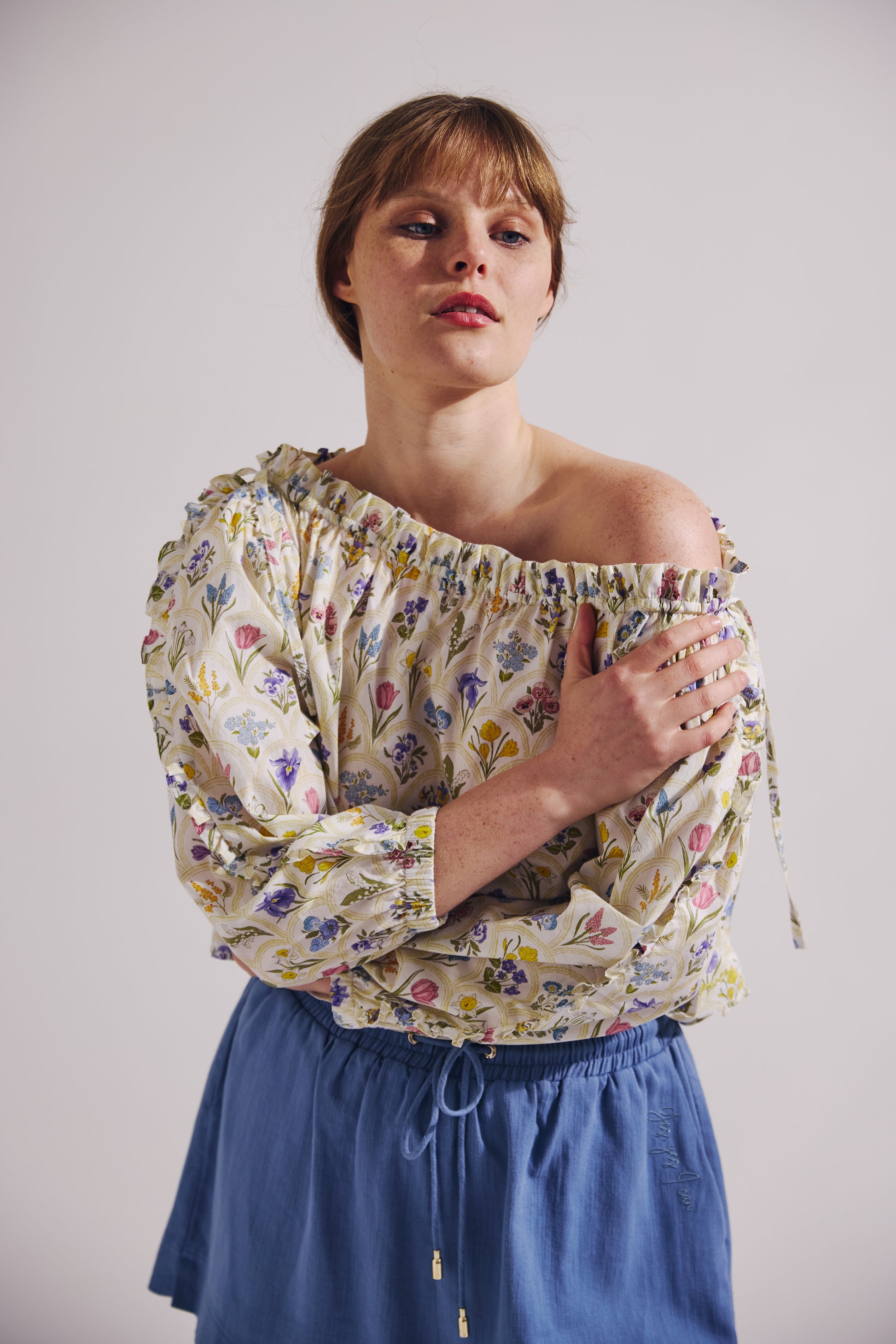 Woman wearing a floral off-shoulder top and blue skirt against a plain background