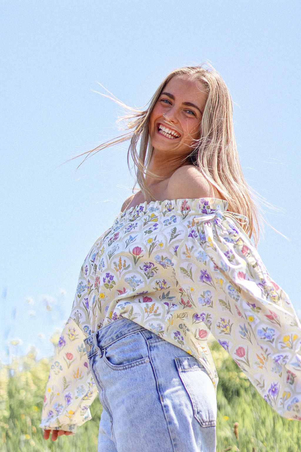 Woman wearing a floral blouse and jeans against a blue sky