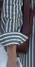 Close-up of a person wearing a green and white striped shirt with a brown leather bag.