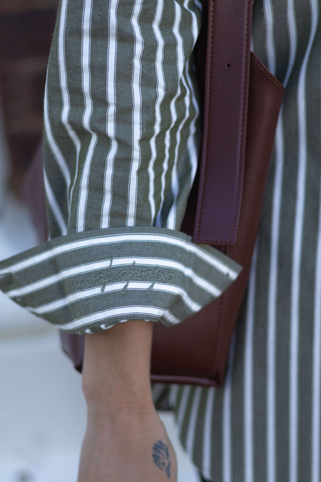 Close-up of a person wearing a green and white striped shirt with a brown leather bag.