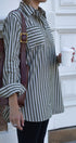 Person wearing a green and white striped shirt holding a brown bag and a white cup.