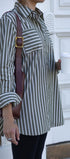 Person wearing a green and white striped shirt holding a brown bag and a white cup.