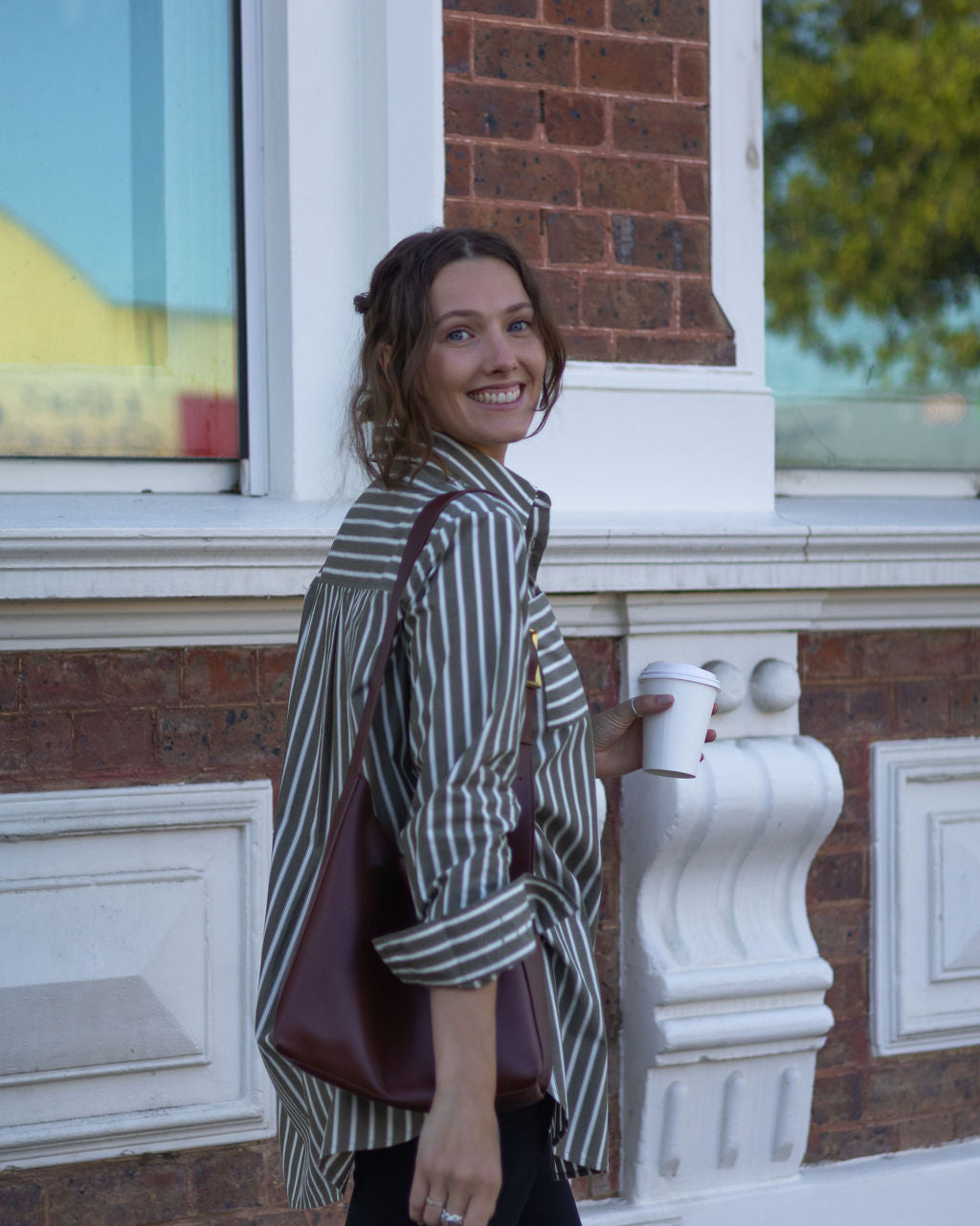 Woman standing outside a building holding a cup and a bag