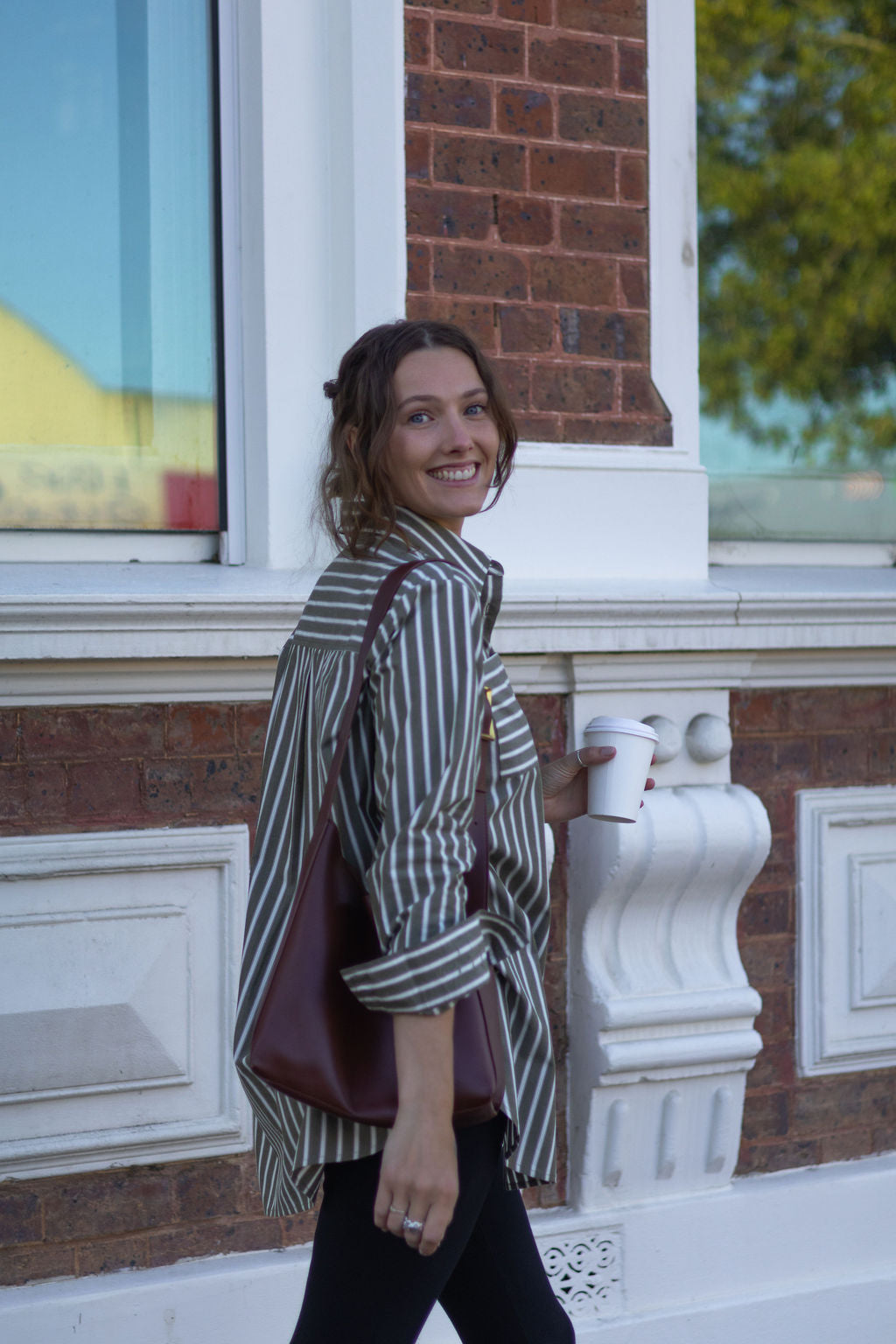 Woman standing outside a building holding a cup and a bag