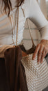 Person holding a woven handbag with a neutral background