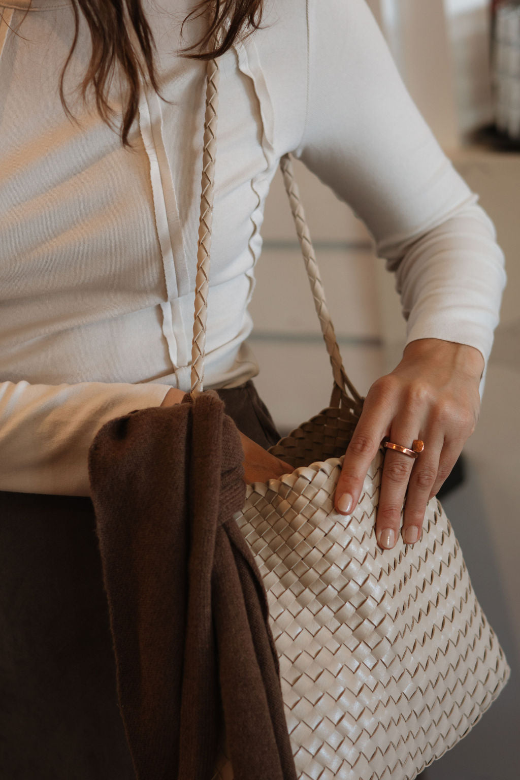 Person holding a woven handbag with a neutral background