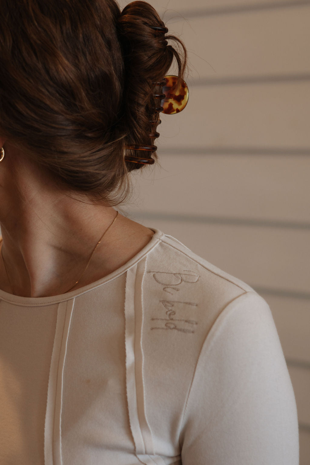 Close-up of a person wearing a beige garment with visible text, against a neutral background.