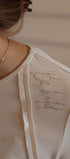 Close-up of a beige garment with 'Du Jour' embroidery on a neutral background
