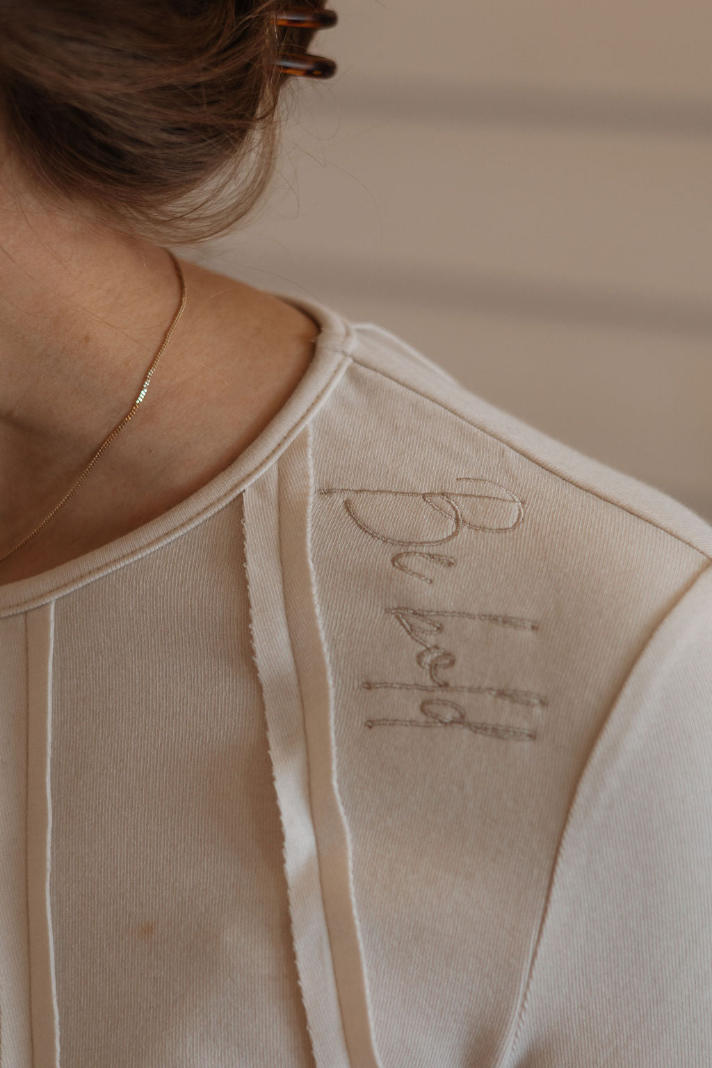 Close-up of a beige garment with 'Du Jour' embroidery on a neutral background