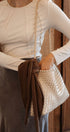 Person holding a woven handbag with a brown ribbon against a wooden background