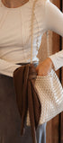 Person holding a woven handbag with a brown ribbon against a wooden background