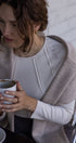 Woman holding a mug with a white shirt and beige cardigan against a light background