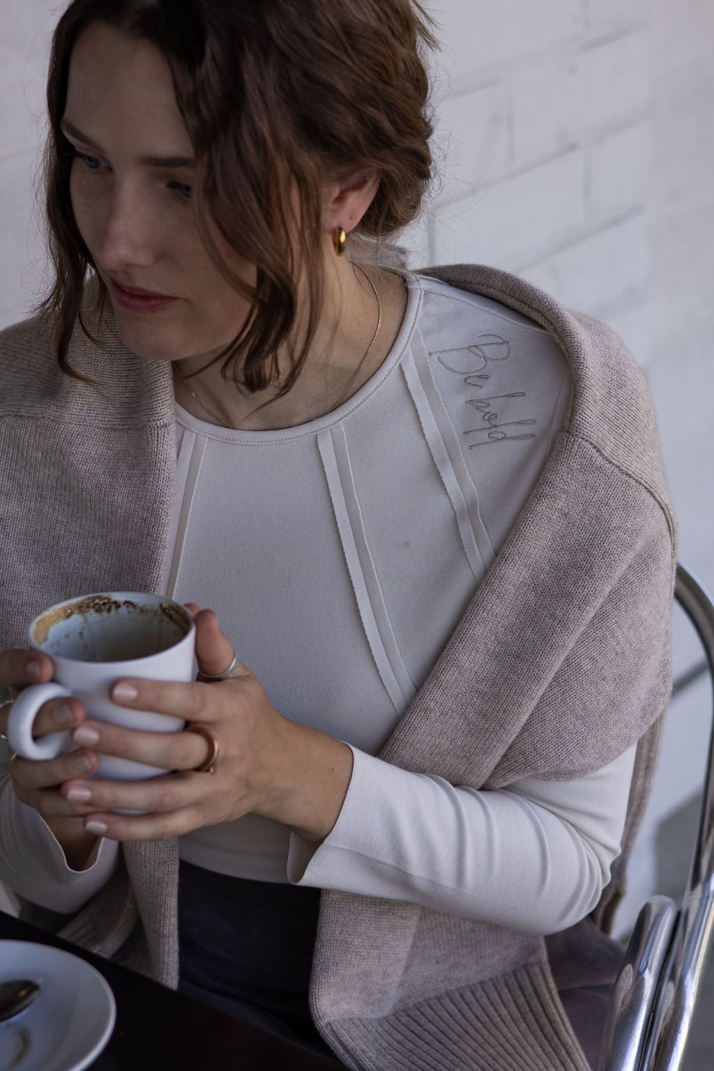 Woman holding a mug with a white shirt and beige cardigan against a light background