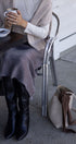 Person sitting at a table with a cup of coffee, wearing a beige sweater and black boots, with a handbag on the ground.