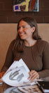 Woman sitting at a table with papers, smiling in a casual setting.