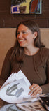 Woman sitting at a table with papers, smiling in a casual setting.