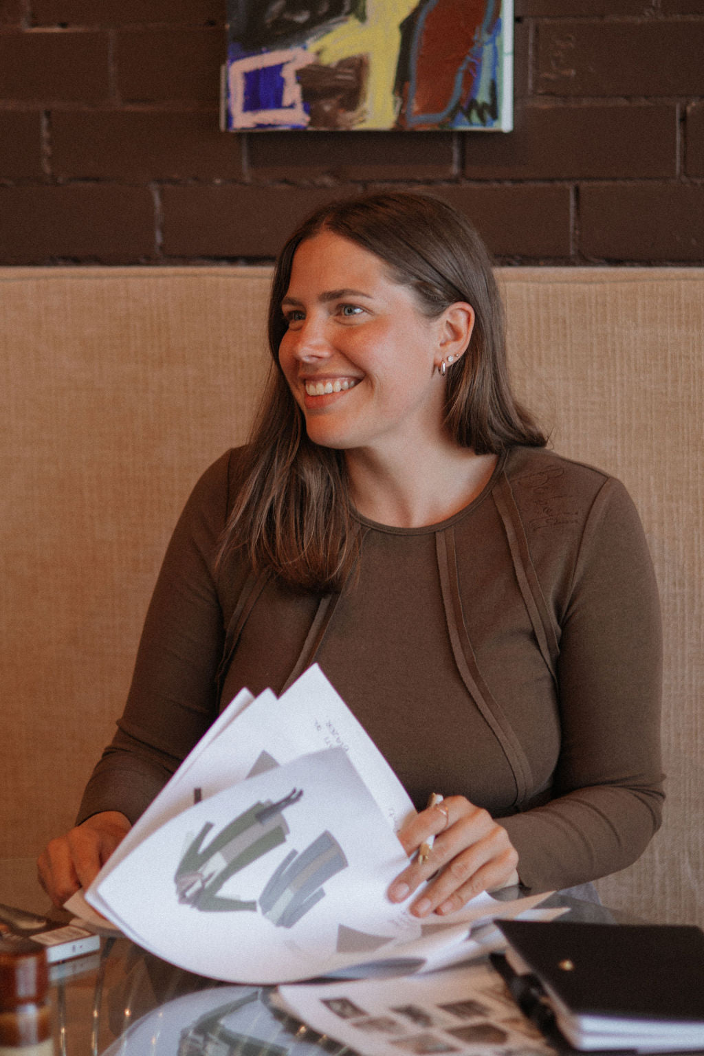 Woman sitting at a table with papers, smiling in a casual setting.