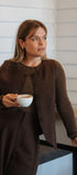Woman in a brown outfit holding a white cup, standing indoors.