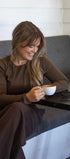 Woman sitting on a gray couch holding a white mug with a striped wall in the background