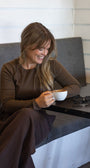 Woman sitting on a gray couch holding a white mug with a striped wall in the background