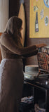 Woman in a kitchen reaching for a plate on a shelf with a colorful painting in the background.