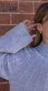 Person wearing a light blue sweater with a brick wall background