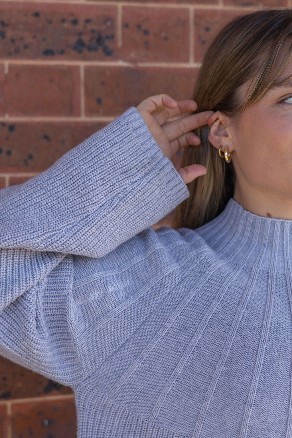 Person wearing a light blue sweater with a brick wall background