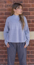 Woman wearing a light blue ribbed sweater and gray pants against a brick wall.