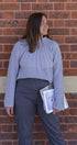 Woman in a gray sweater and dark pants standing against a brick wall
