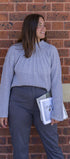Woman in a gray sweater and dark pants standing against a brick wall