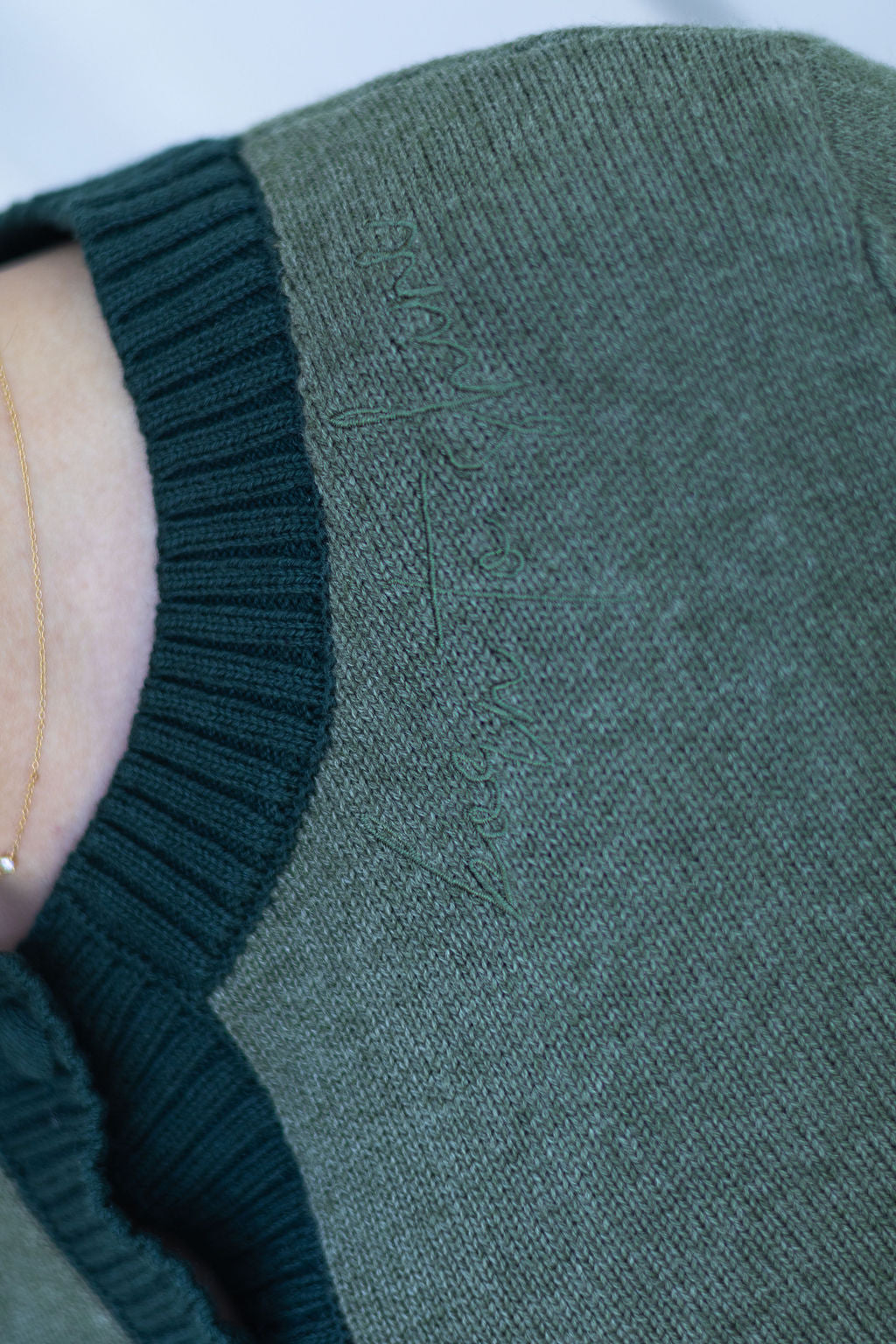 Close-up of a green knitted sweater with embroidered affirmation.