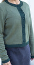 Green cardigan with button details worn by a person on a white background