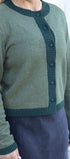 Green cardigan with button details worn by a person on a white background