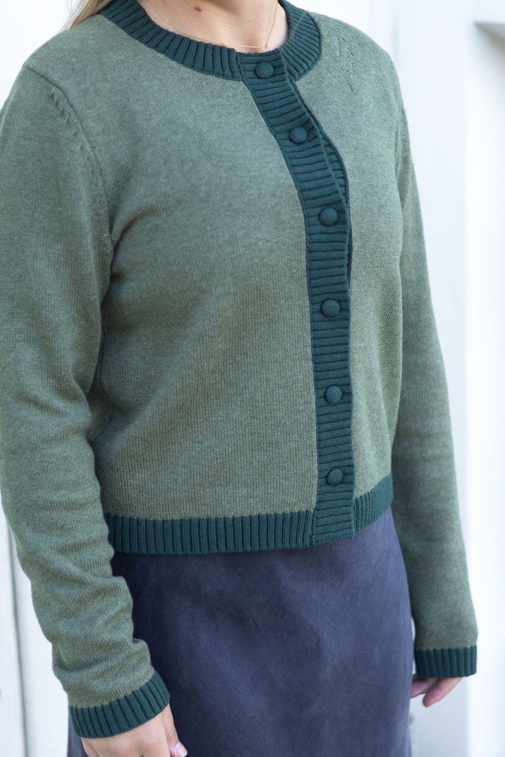 Green cardigan with button details worn by a person on a white background