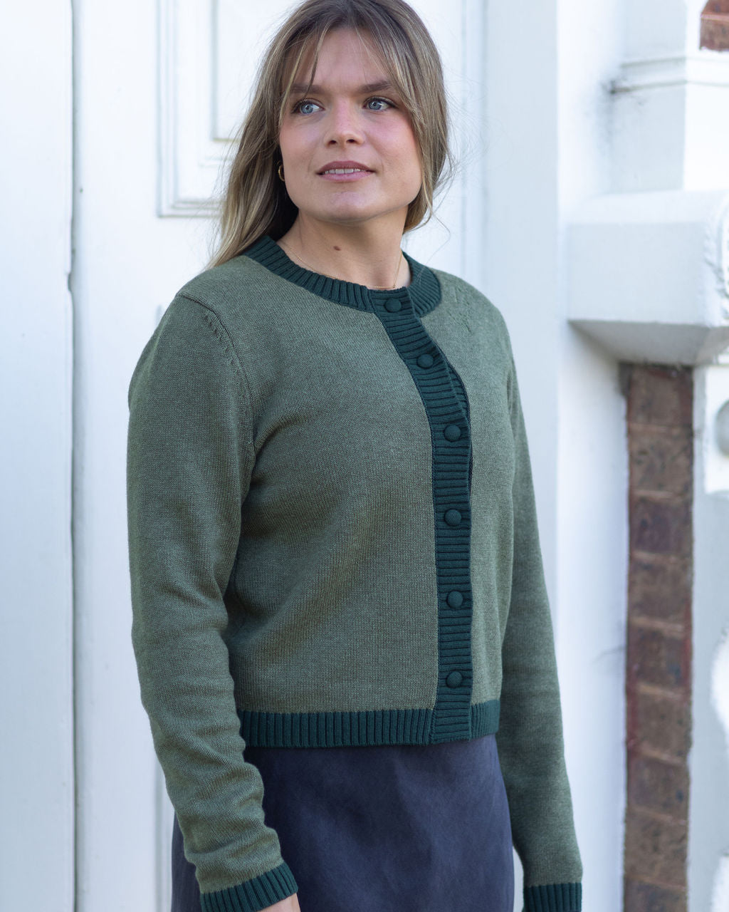 Woman wearing a green sweater standing in front of a white door.
