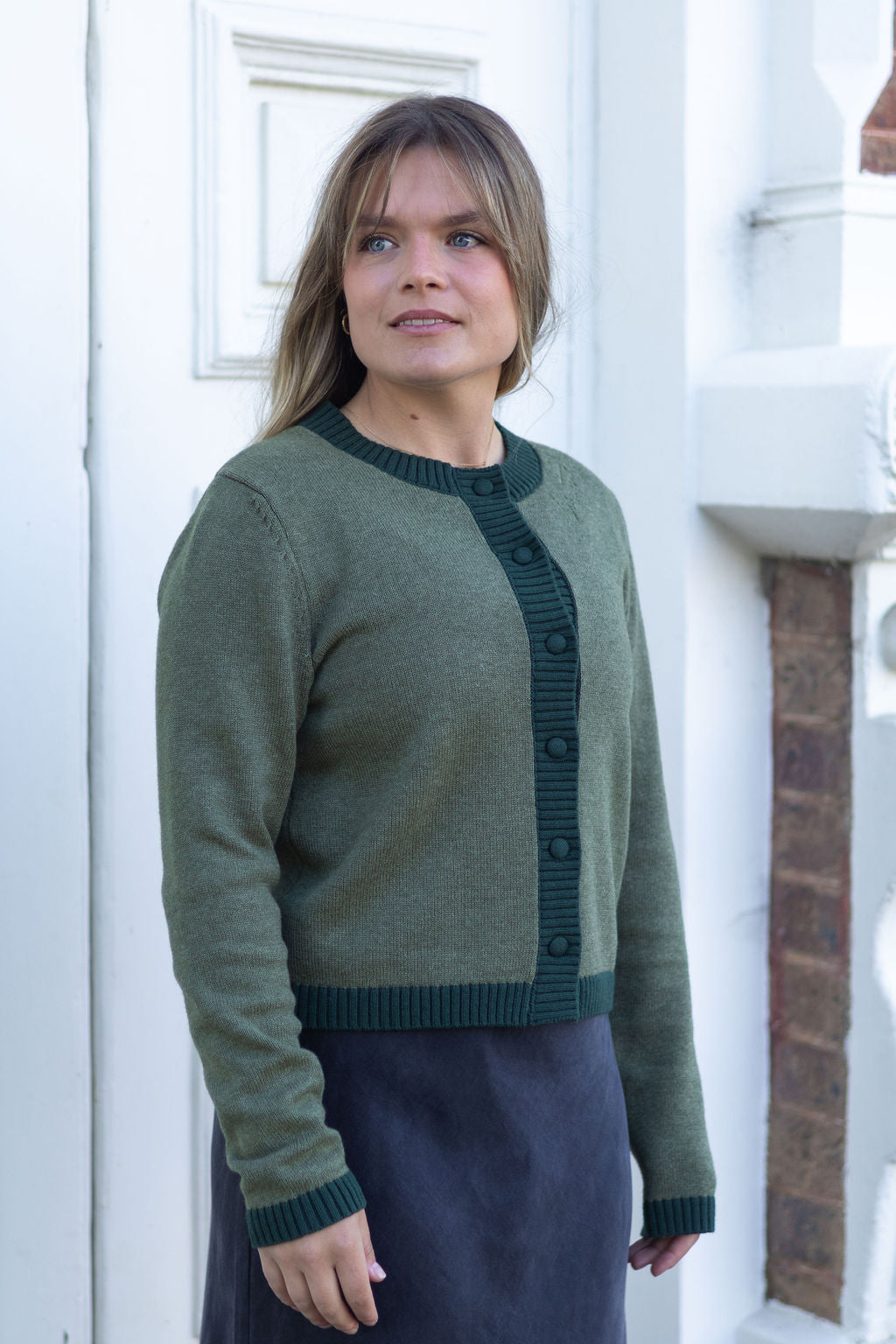 Woman wearing a green sweater standing in front of a white door.