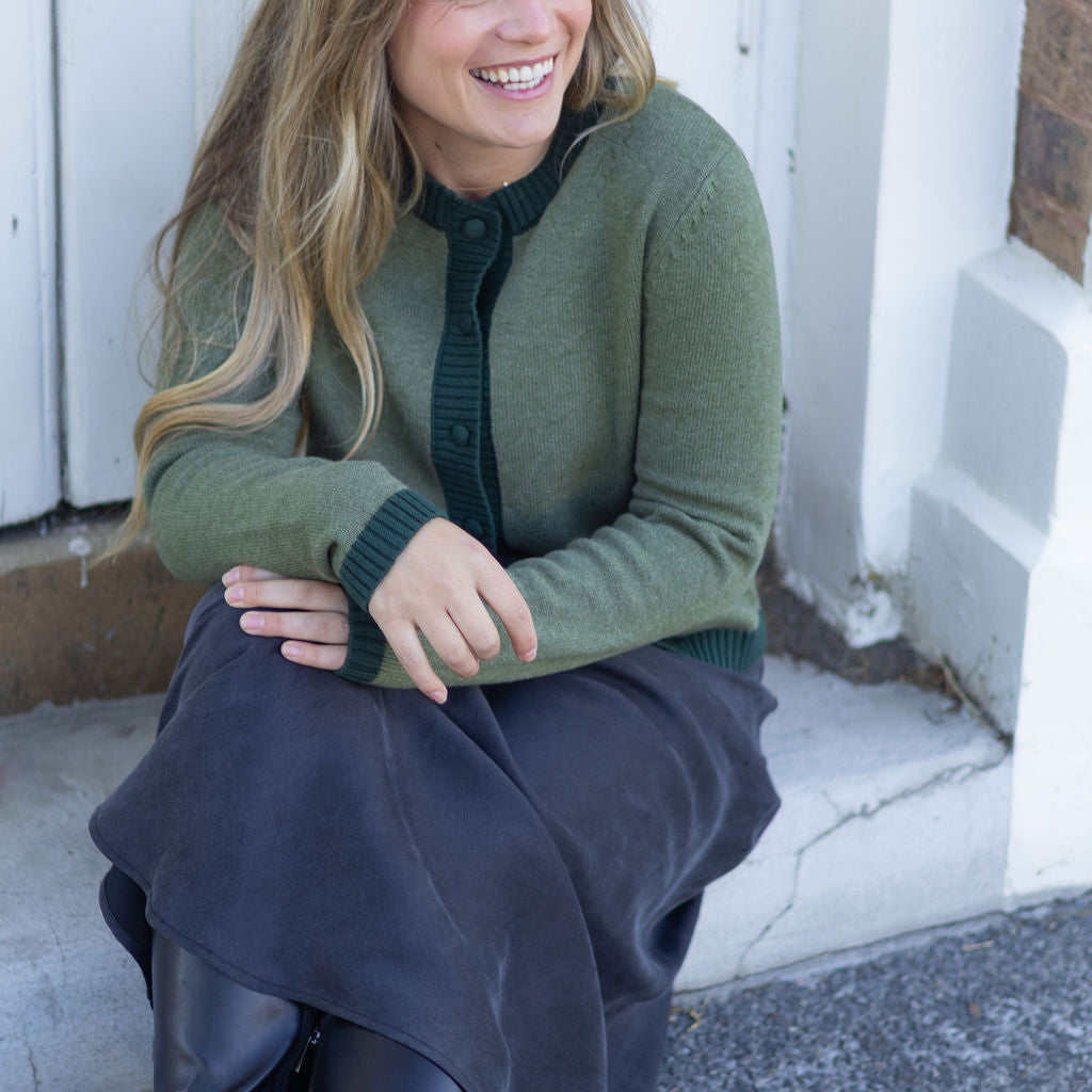 Woman sitting on a step wearing a green sweater and dark pants, smiling.