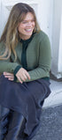 Woman sitting on a step wearing a green sweater and dark pants, smiling.