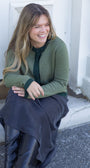 Woman sitting on a step wearing a green sweater and dark pants, smiling.