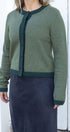 Person wearing a green cardigan over a navy skirt against a white background